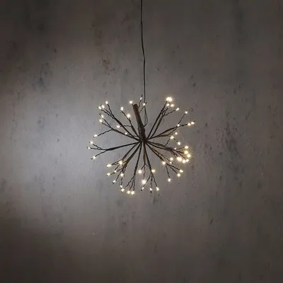 A starburst-shaped light fixture with many small branches, each tipped with a warm white LED, hangs from a wire against a textured gray wall.