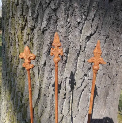 Three decorative iron stakes with fleur-de-lis tops stand in front of a tree trunk.