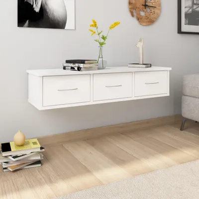 A white wall-mounted drawer unit with books and a vase of flowers on top, set in a room with wooden flooring.
