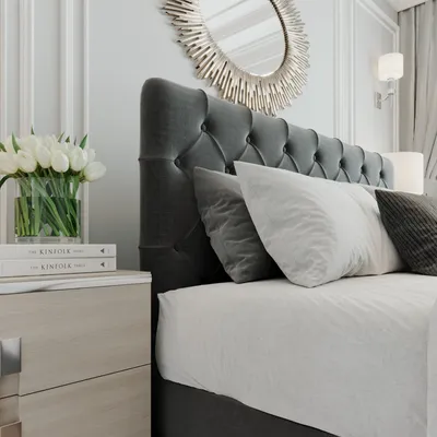 A close-up view of a bedroom setting, focusing on a bed with a tufted headboard, pillows, and a nightstand with flowers.