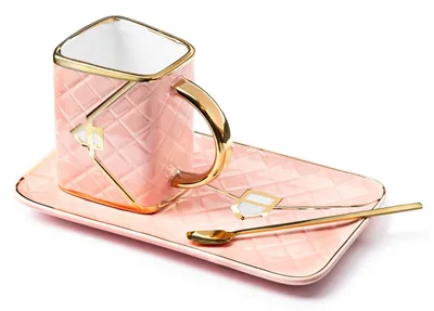 A pink ceramic coffee cup and saucer set with gold accents and two spoons, presented on a white background.