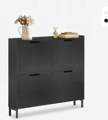 A black shoe cabinet with four flip-out compartments and metal legs, decorated with a vase of flowers and books on top.