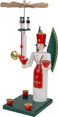 Ein traditioneller hölzerner Engel in rot-weißer Kleidung mit einem Flügel und einer Krone hält eine Trompete und eine Schale während über ihm ein Propeller mit kleinen Figuren schwebt und auf einem grünen Sockel vier Kerzenhalter stehen