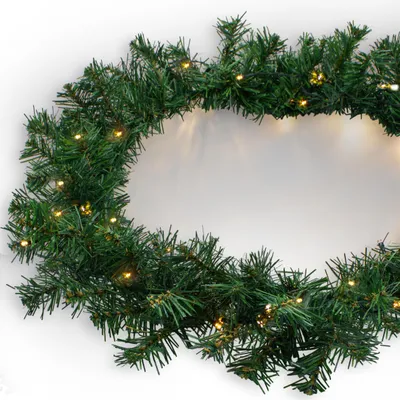 A close-up of a green artificial Christmas garland with warm white LED lights, arranged in a curve against a white background.