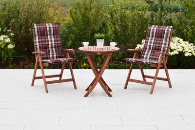 A wooden garden furniture set with two chairs and a table on a paved patio, surrounded by greenery.