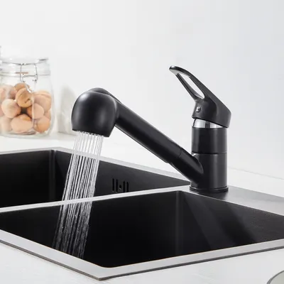 A black kitchen faucet with a pull-out sprayer is shown in use, with water running into a double black sink. A glass jar filled with nuts is visible in the background.