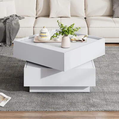 A white rotating coffee table with decorative items on top, placed on a gray rug in front of a white sofa.