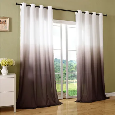 Two ombre curtains hanging in front of a window with a view of greenery.