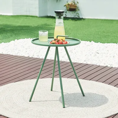 An outdoor side table with a drink and strawberries on it, set on a deck with a lawn and white pebbles in the background.