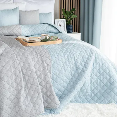 A neatly made bed with a blue quilted bedspread and a gray throw blanket.
