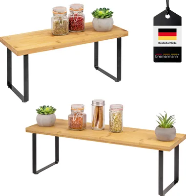 Two bamboo kitchen shelves with black metal legs, one above the other, each displaying jars and small plants.