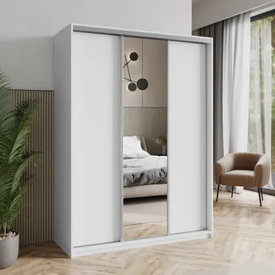 A white sliding door wardrobe with a mirror in the center, placed in a bedroom setting with a bed visible in the reflection. A chair and a plant are also visible.