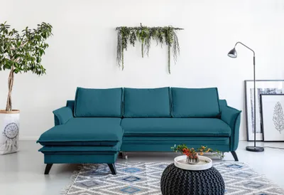 A teal sectional sofa is shown in a well-lit room with a plant and a floor lamp.