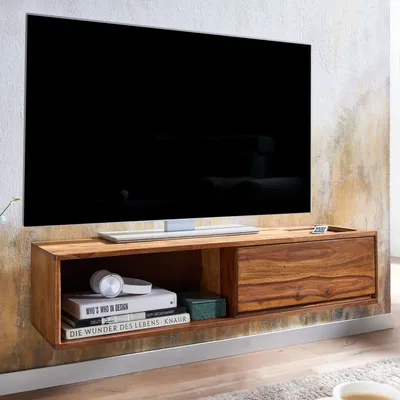 A modern, wall-mounted wooden TV stand with a television on top, placed against a textured wall.