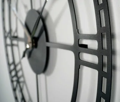 A close-up, angled view of a black metal wall clock with a vintage, industrial design.