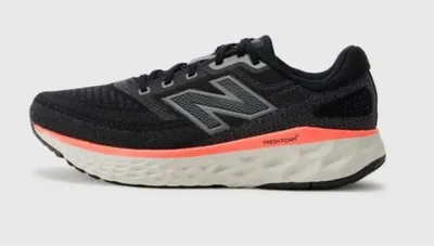 A side view of a black New Balance running shoe with a coral and white sole.
