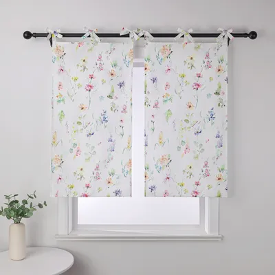 A pair of tie-top cafe curtains with a floral pattern hang on a window.