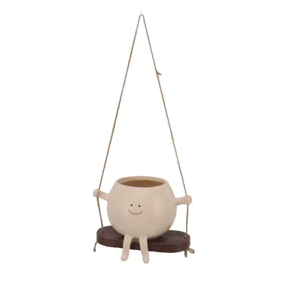 A hanging planter shaped like a round character with a smiley face, sitting on a swing.