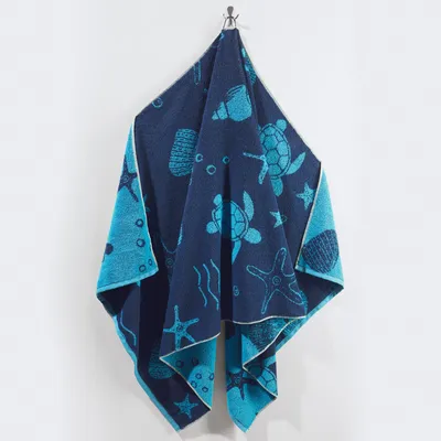 A beach towel with a marine-themed pattern is hanging on a hook against a white wall.