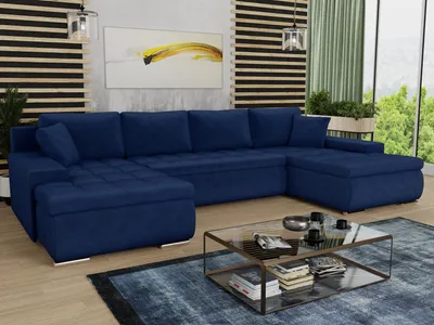 A spacious living room with a large U-shaped blue sofa, a glass coffee table, and a large window overlooking greenery.
