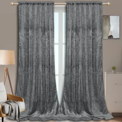 A pair of gray velvet curtains with a damask pattern hang in front of a window, with a chair and a dresser visible in the background.