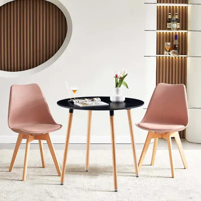 A modern dining set with a round black table and two pink chairs, set in a well-lit room with decorative shelving in the background.