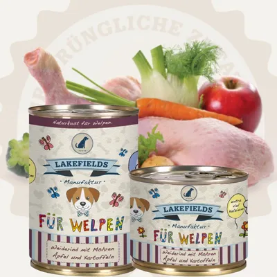Two cans of dog food are shown in front of a background of raw ingredients like chicken, carrots, fennel, and an apple. The cans have colorful labels with illustrations of dogs and butterflies.