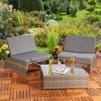 A garden lounge set with two armchairs and a coffee table on a wooden deck, surrounded by a lush garden with flowers and a decorative windmill.