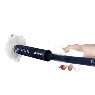 A hand is holding a black corrugated tube with a cable inside, and it is being inserted into a white circular object. The tube has text printed on it.