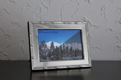 A silver digital picture frame displaying a winter landscape with text overlays indicating its status.