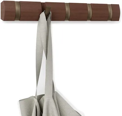 A wooden coat rack with five hooks is mounted on a white wall. A light gray bag is hanging from one of the hooks.