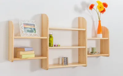 Three wooden shelves mounted on a white wall, decorated with books, a bottle, candles, a vase with flowers, and a framed picture.