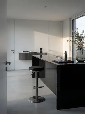 Schwarzer Barhocker aus Edelstahl an einer freistehenden Kücheninsel aus Pietra Grigia Marmor im modernen Architekturhaus mit Betonwand._#sku_SAFWL1.293#