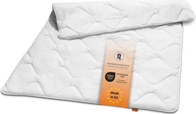 A white quilted comforter is folded and laid flat on a white background. A small orange tag with text and logos is placed on top of the comforter.