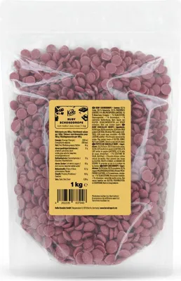 A clear plastic bag filled with small, pink, disc-shaped ruby chocolate drops. A yellow label with product information is attached to the front of the bag.