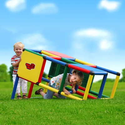 Two children playing on a modular climbing frame in a grassy outdoor area with a blue sky and clouds.