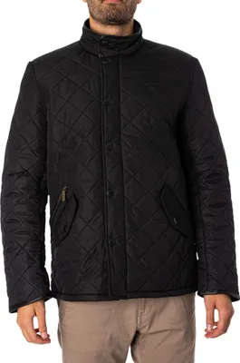 A man wearing a black quilted jacket and tan pants.