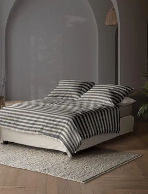 A neatly made bed with striped bedding in a room with arched walls and soft lighting.