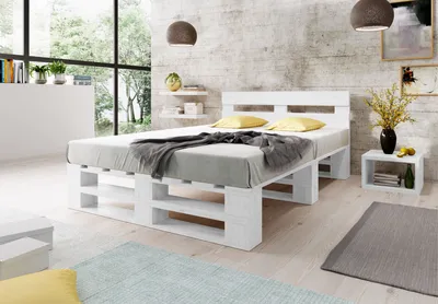 A modern bedroom with a white pallet bed, yellow pillows, and a grey blanket.