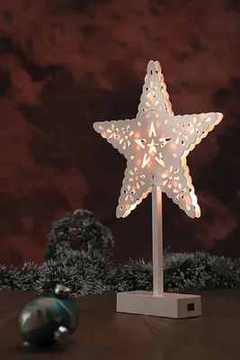 A decorative star lamp with intricate cutouts, placed on a wooden surface with Christmas decorations in the background.
