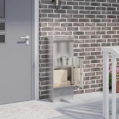 A parcel drop box with two packages inside, placed on a patio next to a gray door and a brick wall.