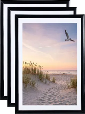 Three black picture frames are stacked on top of each other, with the front frame displaying a beach scene at sunset.