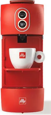 A red Illy capsule coffee machine with a white Illy cup on the shelf.