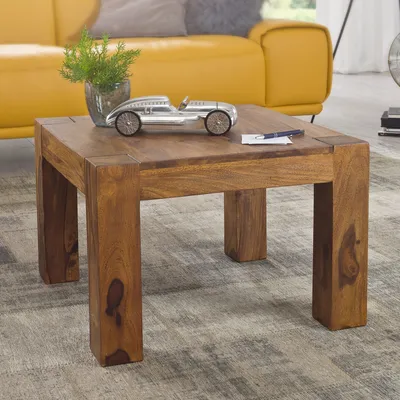 A wooden coffee table with a decorative car and plant on it, in a living room setting with a yellow sofa in the background.
