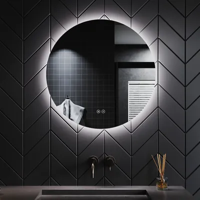 A modern bathroom with a round LED mirror mounted on a dark, chevron-patterned tiled wall above a sink.