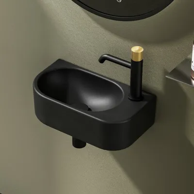 A close-up shot of a black ceramic corner wall-mounted sink with a black faucet with a gold accent.
