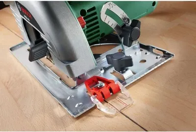 Close-up of a Bosch circular saw with a red accessory attached to the base plate, resting on a wooden surface.