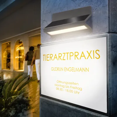 A sign for a veterinary practice is illuminated by a modern outdoor light fixture.