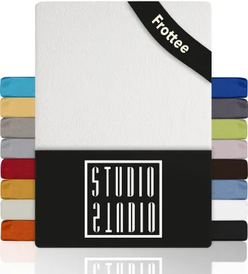 A white fitted sheet with a black band at the bottom displaying the brand logo. Several swatches of different colored fitted sheets are stacked on the left and right sides.