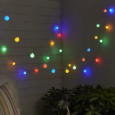 A string of colorful LED party lights is draped along a wooden wall and a darker wall, with some greenery visible at the bottom.